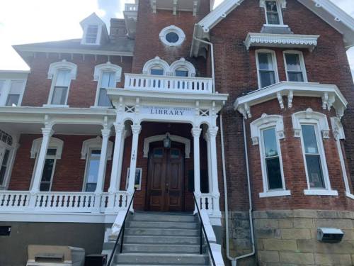 Historic brick library building with ornate white trim and a grand entrance. Steps lead up to the front door.
