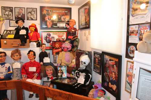 A collection of puppets and ventriloquist dummies displayed in a museum, surrounded by framed posters and memorabilia.