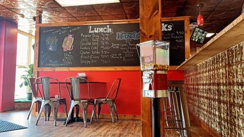 A cozy eatery with a chalkboard menu, metal chairs, and a gumball machine in a warm, inviting atmosphere.