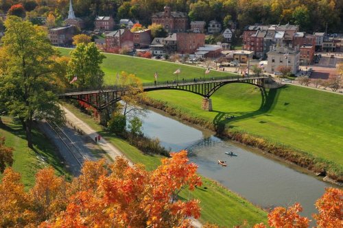 A scenic view of a town with a bridge over a river, surrounded by autumn foliage and colorful buildings.