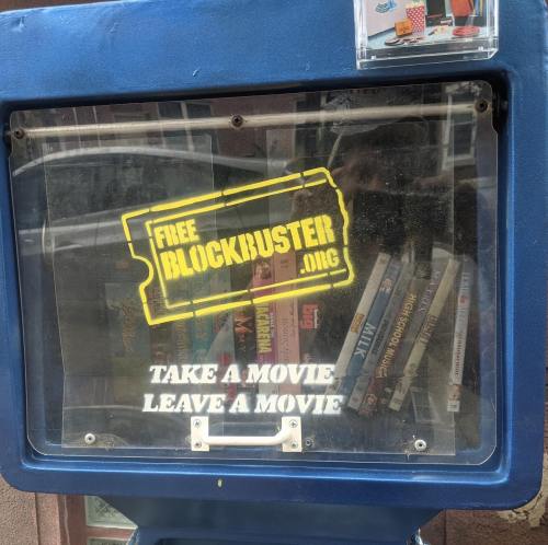 A blue movie rental box with a "Free Blockbuster" sign, inviting users to take or leave a movie.