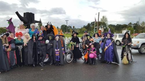 A group of people dressed in various witch costumes, posing together in a festive outdoor setting.