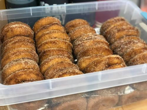 A clear container filled with neatly arranged, sugar-coated donuts.