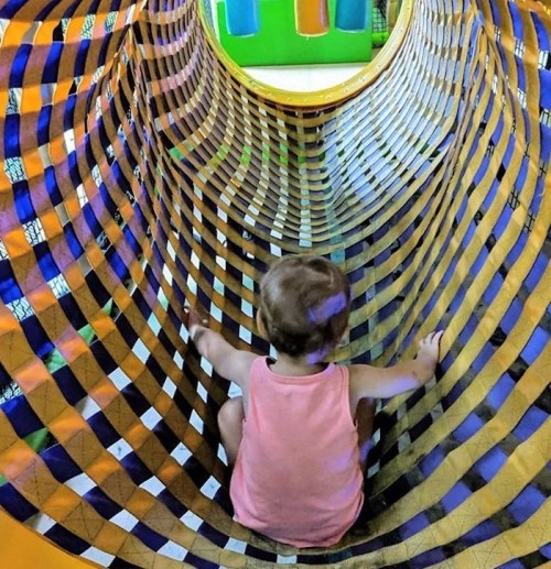 A child sits inside a colorful, patterned tunnel at a play area, exploring the vibrant surroundings.