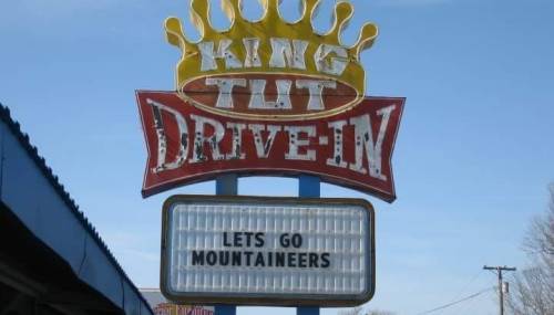 Sign for King Tut Drive-In with a marquee reading "LET'S GO MOUNTAINEERS" against a clear blue sky.