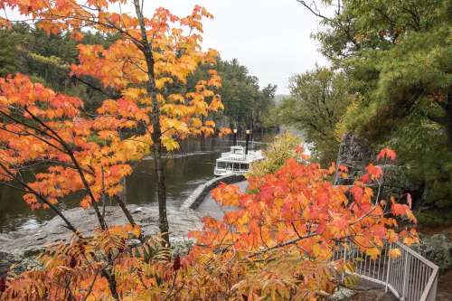 A scenic view of a river surrounded by vibrant autumn foliage and a boat docked nearby.