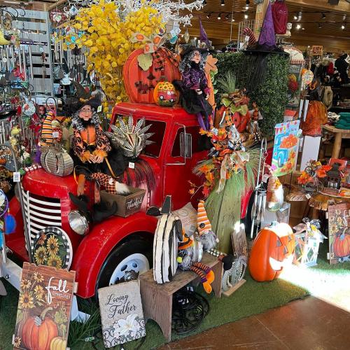 A vibrant display of fall decorations featuring a red truck, pumpkins, witches, and autumn-themed decor.