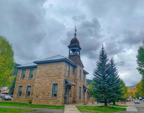 Historic stone building with a bell tower, surrounded by trees and cloudy skies.