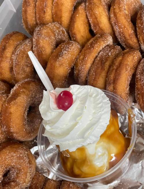 A cup of ice cream topped with whipped cream and a cherry, surrounded by a pile of cinnamon sugar donuts.