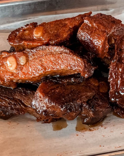 A close-up of succulent, glazed beef ribs arranged on a tray, glistening with sauce and garnished with garlic.