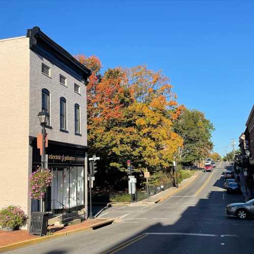 A quaint street scene featuring a brick building, colorful autumn trees, and a clear blue sky.