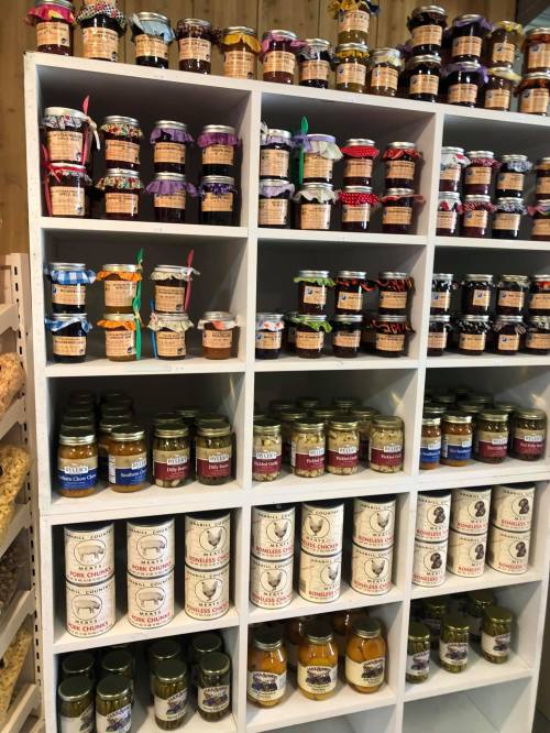 A neatly organized shelf displaying various jars of preserves and sauces, each with colorful labels and lids.