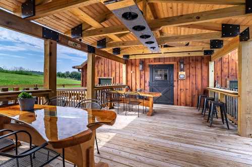 A wooden deck with tables and chairs, featuring a rustic design and open view of green fields.