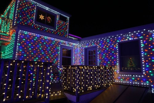 A brightly lit house decorated with colorful Christmas lights, featuring a visible tree in the window.