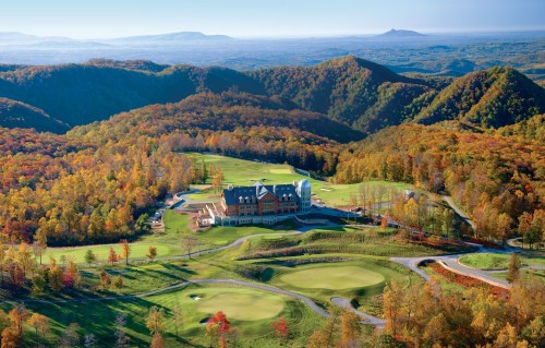 Aerial view of a golf course and resort surrounded by colorful autumn foliage and rolling mountains.