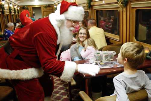 Santa Claus interacts with a child on a festive train, while families enjoy the holiday atmosphere around them.