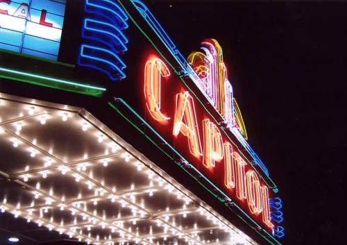 Brightly lit Capitol theater marquee at night, featuring colorful neon lights and decorative bulbs.
