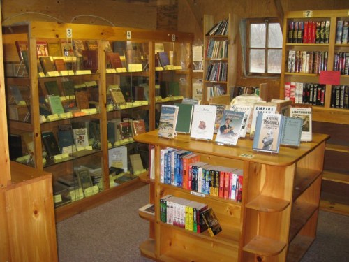 A cozy library interior featuring wooden shelves, display cases of books, and a central wooden bookstand.