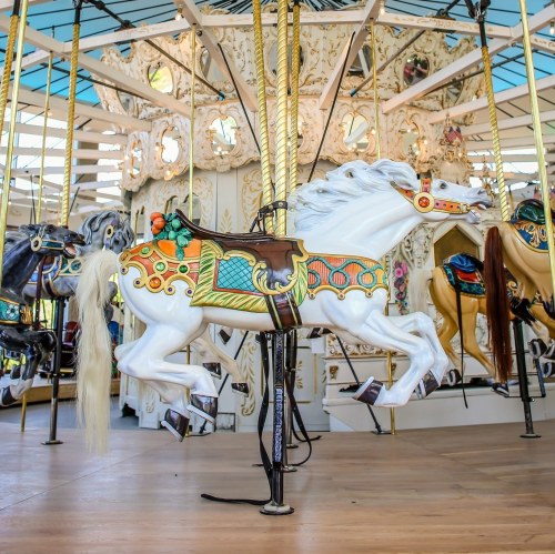 A colorful carousel with a white horse in motion, surrounded by ornate decorations and other carousel animals.