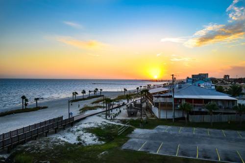 Sunset over a beach with palm trees, a pier in the distance, and a coastal building along the shore.