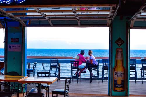 Two people sit at a bar overlooking the ocean, enjoying the view from a seaside deck.