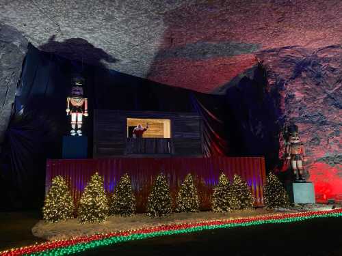 A festive display in a cave featuring nutcracker figures, a stage, and decorated trees with colorful lights.