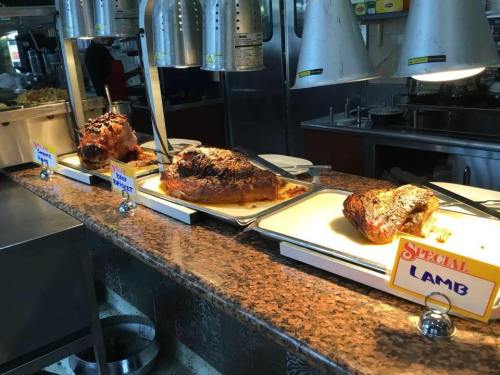 A buffet display featuring roasted lamb and other meats on a serving counter with labels.