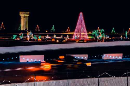 Colorful holiday lights decorate a highway at night, featuring a large pink Christmas tree and festive displays.