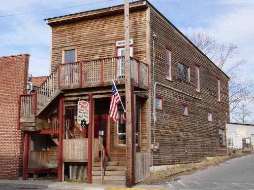 A weathered wooden building with a staircase, featuring a sign and an American flag outside.