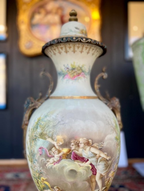 A decorative vase featuring intricate painted scenes of cherubs and classical figures, set against a dark background.