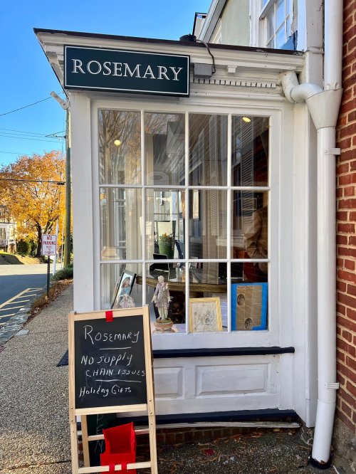 A storefront with a sign reading "Rosemary" and a chalkboard stating "No Supply Chain Issues. Holiday Gifts."