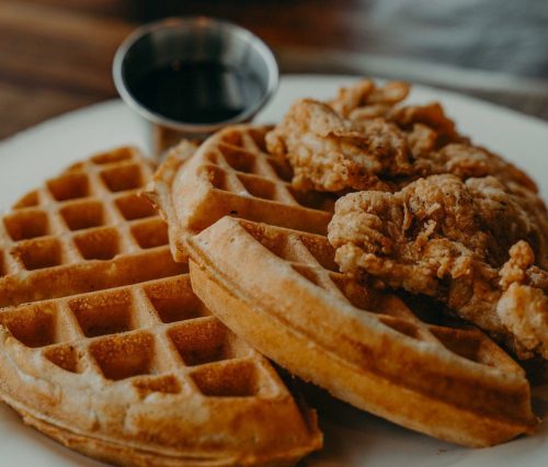 A plate of golden waffles topped with crispy fried chicken and a small cup of syrup on the side.