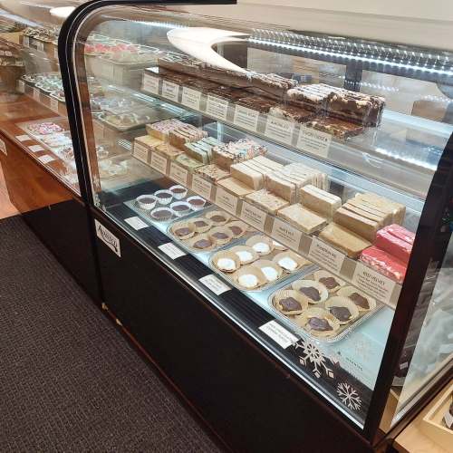 A display case filled with various desserts, including cakes, cookies, and bars, neatly arranged and labeled.