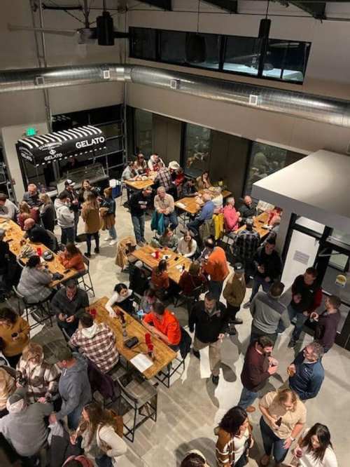 A crowded indoor venue with people socializing at tables, enjoying food and drinks in a lively atmosphere.