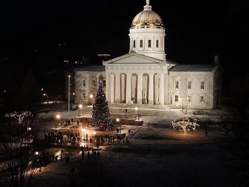 A festive scene at night featuring a lit Christmas tree in front of a grand building with a dome, surrounded by holiday lights.