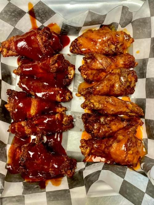 A tray of chicken wings, half coated in barbecue sauce and half with a spicy glaze, on a checkered paper liner.