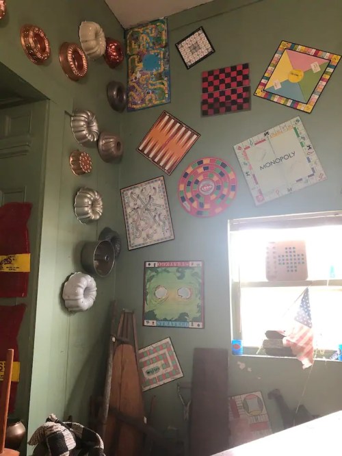 A green wall adorned with various vintage game boards and baking molds, with a window showing an American flag.