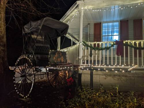 A decorated horse-drawn carriage sits beside a house adorned with festive lights and greenery.