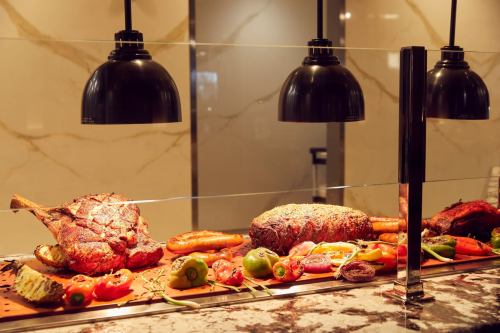 A display of roasted meats and colorful vegetables under black pendant lights on a marble countertop.
