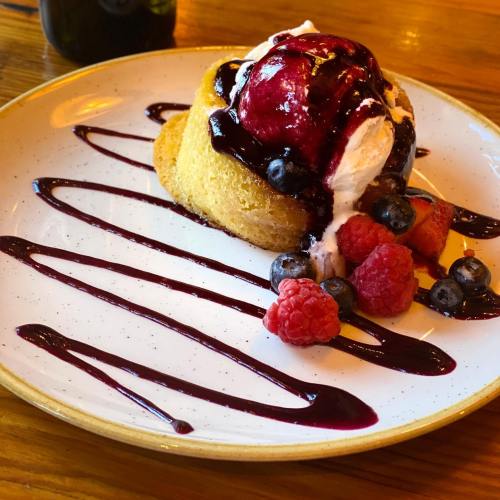 A dessert featuring a cake topped with ice cream, berries, and berry sauce, served on a white plate.