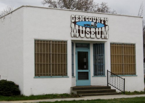 Exterior of the Gem County Museum, featuring a white building with barred windows and a blue door.