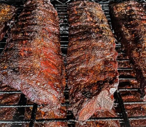 Close-up of smoked ribs on a grill, showcasing a dark, caramelized crust and juicy texture.