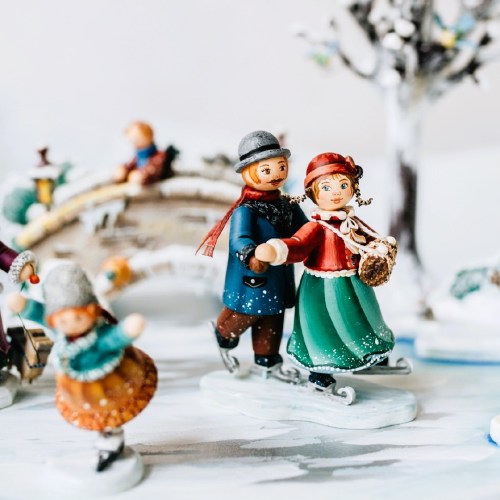 A festive scene featuring miniature figurines of a couple ice skating, surrounded by snowy decorations and trees.