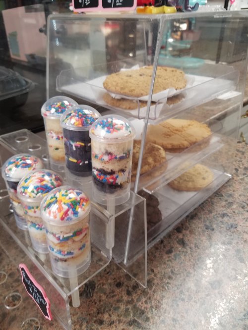 A display case with colorful dessert cups and cookies, featuring sprinkles and layered treats.