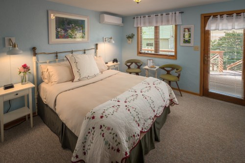 Cozy bedroom with a bed, decorative quilt, and windows overlooking a deck, featuring soft lighting and a welcoming atmosphere.