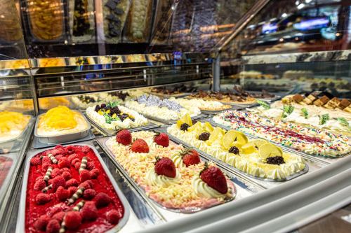 A display of colorful gelato and desserts, featuring various flavors topped with fruits and sprinkles.