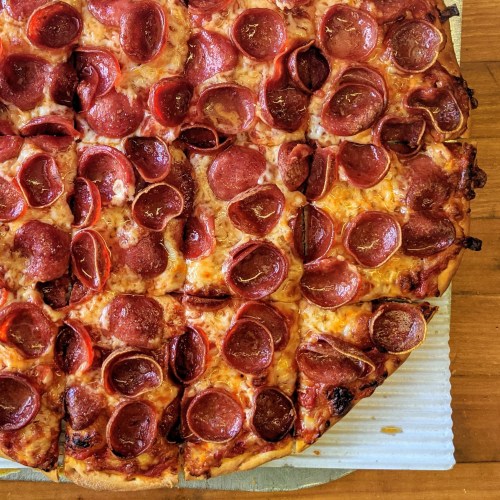 A large pepperoni pizza with a golden crust and abundant slices of pepperoni on top, placed on a wooden table.