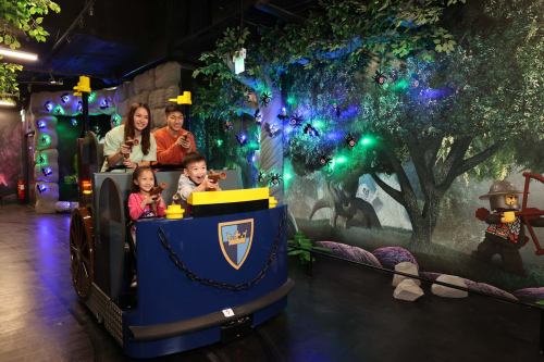 A family enjoys a ride in a colorful, themed attraction with a forest backdrop and playful decorations.