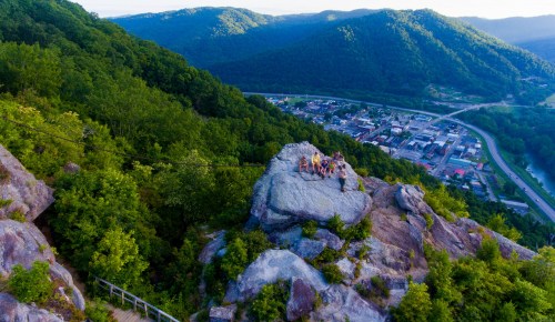 Aerial view of a group of people on a rocky outcrop overlooking a lush green valley and a small town below.