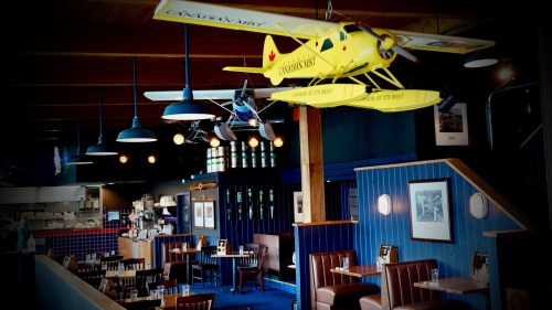 Interior of a restaurant featuring yellow biplane decor, wooden tables, and blue walls with framed photos.